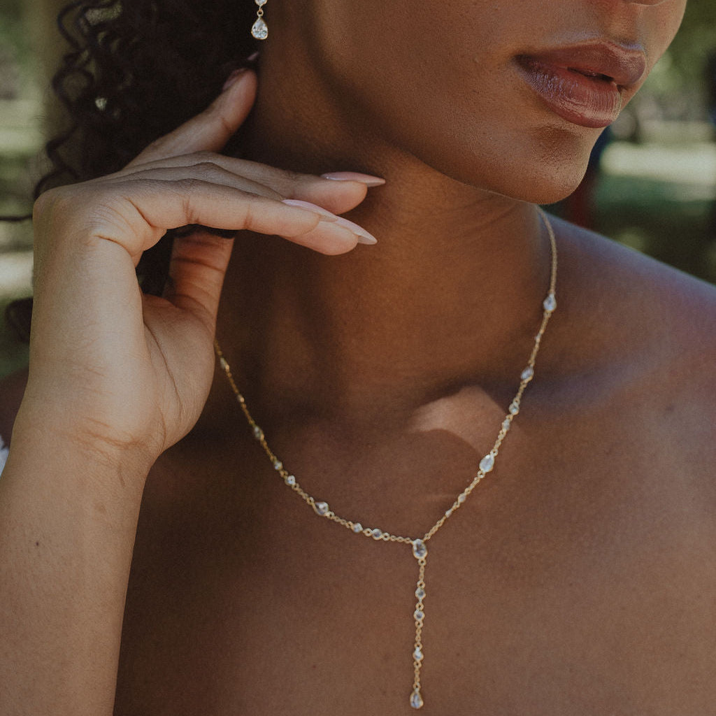 Close-up of a woman wearing a delicate necklace and earrings with a blurred natural background